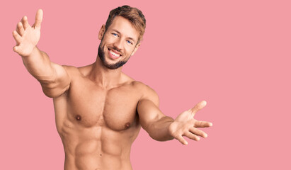 Fototapeta premium Young caucasian man standing shirtless looking at the camera smiling with open arms for hug. cheerful expression embracing happiness.