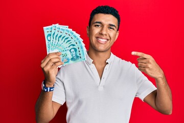 Young arab man holding yuan chinese banknotes smiling happy pointing with hand and finger