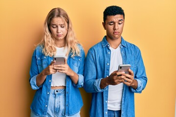 Young interracial couple using smartphone skeptic and nervous, frowning upset because of problem. negative person.