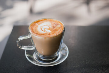 Cappuccino with crema in a transparent cup on black desk, latte art concept and Cafe culture.