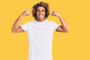 Fototapeta na wymiar Young hispanic man wearing casual white tshirt smiling pointing to head with both hands finger, great idea or thought, good memory