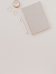 feminine desk workspace with notebook on dusty pink background.