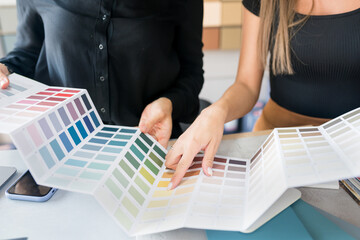 
Close-up of two women choosing samples of wall paint. Interior designer consulting a client looking at a color swatch