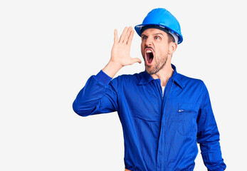 Young handsome man wearing worker uniform and hardhat shouting and screaming loud to side with hand on mouth. communication concept.