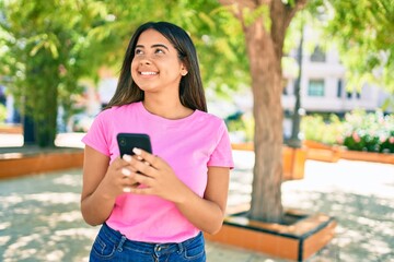 Young latin woman smiling happy using smartphone at the city.