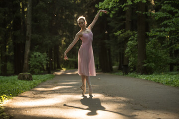Backlit silhouette of young ballerina dancing in the park with dancing shadow on the ground (selective focus)