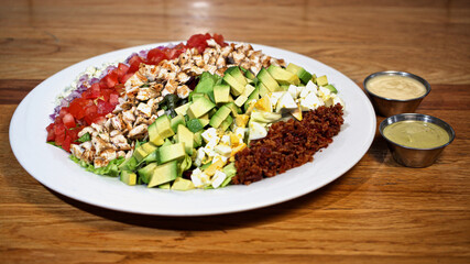 Ensalada mixta. Pollo, aguacate, huevo, tocino, jitomate, cebolla, queso azul sobre mesa de madera