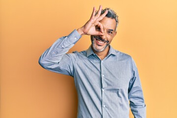 Middle age grey-haired man wearing casual clothes smiling happy doing ok sign with hand on eye looking through fingers