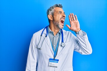 Middle age grey-haired man wearing doctor uniform and stethoscope shouting and screaming loud to...