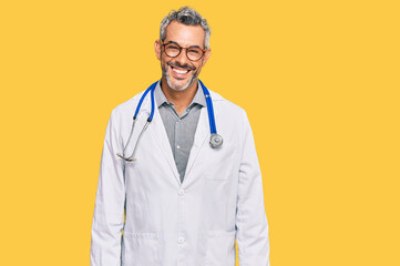 Middle age grey-haired man wearing doctor uniform and stethoscope looking positive and happy...