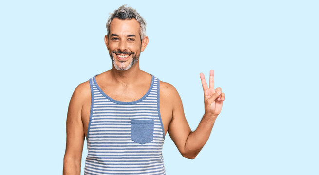 Middle age grey-haired man wearing casual style with sleeveless shirt smiling with happy face winking at the camera doing victory sign. number two.