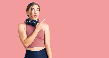 Obraz premium Beautiful caucasian young woman wearing gym clothes and using headphones surprised pointing with finger to the side, open mouth amazed expression.