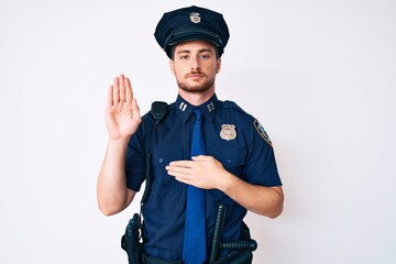 Young caucasian man wearing police uniform swearing with hand on chest and open palm, making a loyalty promise oath