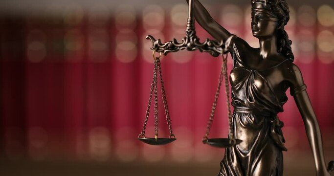 bronze law statue represented by blindfolded goddess spinning and holding a balance signifying impartiality and two broad sources of law in a university room with a background made of books