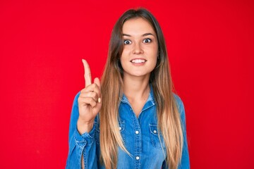 Beautiful caucasian woman wearing casual denim shirt smiling with an idea or question pointing finger up with happy face, number one