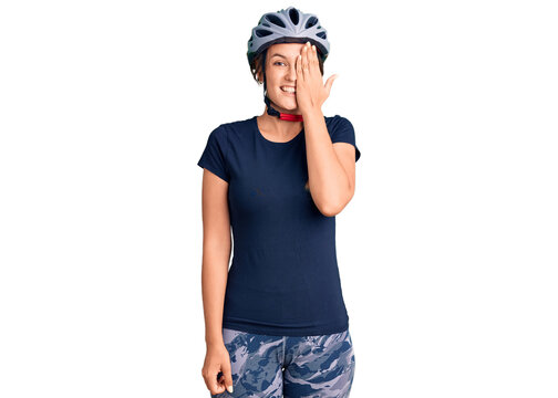 Beautiful caucasian woman wearing bike helmet covering one eye with hand, confident smile on face and surprise emotion.