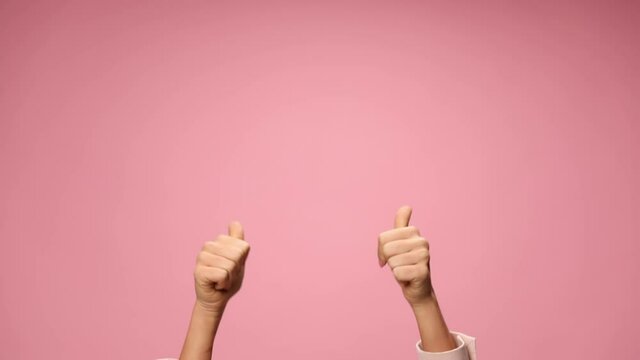 young woman holding hands in the air pointing fingers, moving, making thumbs up gesture on pink background