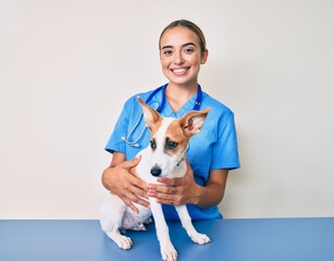 Young beautiful blonde veterinarian woman checking dog health looking positive and happy standing...