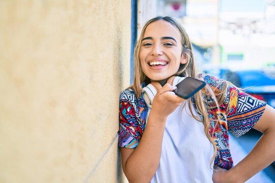 Young beautiful blonde caucasian woman smiling happy outdoors on a sunny day wearing headphones and using smartphone