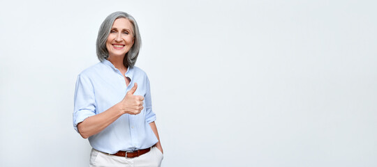 Smiling older mature businesswoman employer showing thumbs up like hand gesture standing isolated...