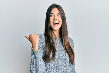 Young brunette woman wearing casual winter sweater pointing thumb up to the side smiling happy with open mouth