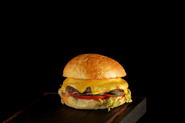Delicious homemade burger on dark wooden cutting board, close-up. Black background, copy space