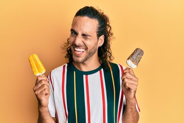 Young handsome man with long hair eating two ice cream winking looking at the camera with sexy...