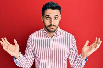 Naklejka premium Young hispanic man wearing business shirt clueless and confused with open arms, no idea and doubtful face.