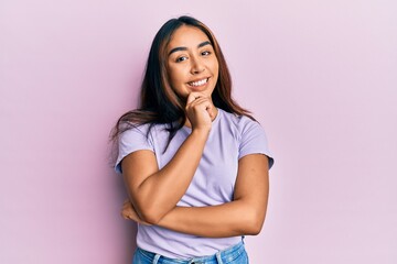 Young latin woman wearing casual clothes smiling looking confident at the camera with crossed arms and hand on chin. thinking positive.