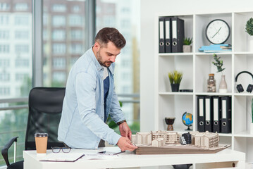 Handsome bearded architect working on a construction project, he examines the model on which he works