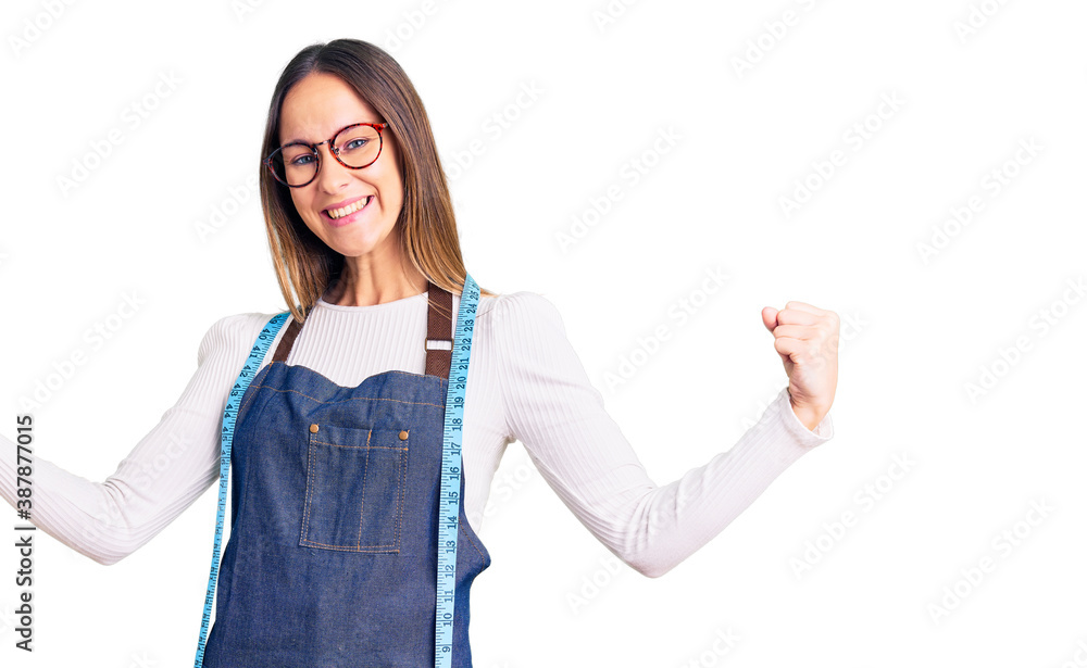 Wall mural beautiful brunette young woman dressmaker designer wearing atelier apron very happy and excited doin