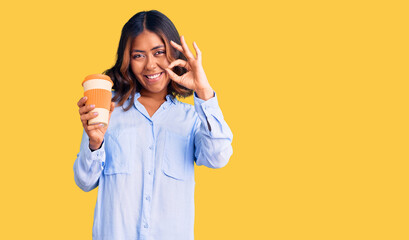 Young beautiful mixed race woman drinking a coffee from take away cup doing ok sign with fingers, smiling friendly gesturing excellent symbol