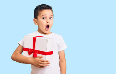 Little cute boy kid holding gift scared and amazed with open mouth for surprise, disbelief face