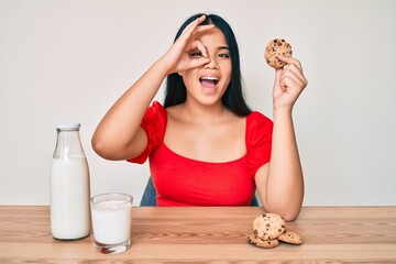 Young beautiful asian girl drinking a glass of fresh milk with chocolate cookies smiling happy...