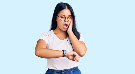 Young beautiful asian girl wearing casual clothes and glasses looking at the watch time worried, afraid of getting late