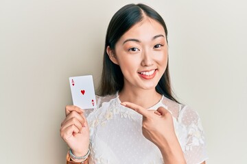 Young chinese woman holding ace poker card smiling happy pointing with hand and finger