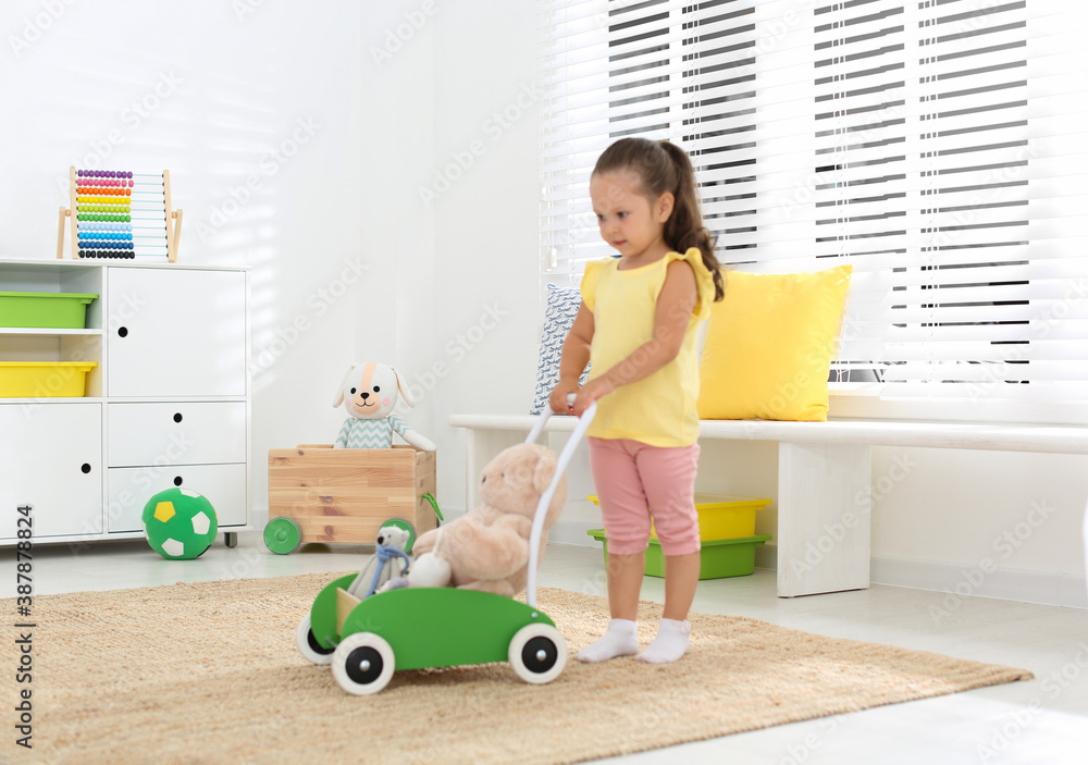 Poster cute little girl playing with toy walker and teddy bear at home