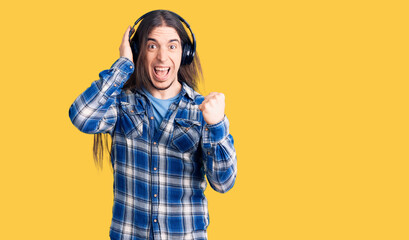 Young adult man with long hair listening to music using headphones screaming proud, celebrating victory and success very excited with raised arms