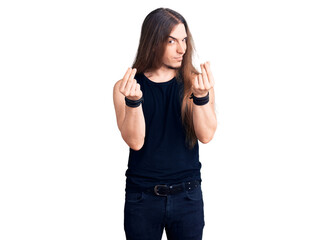 Young adult man with long hair wearing goth style with black clothes doing money gesture with...