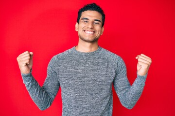 Young handsome hispanic man over red background screaming proud, celebrating victory and success...