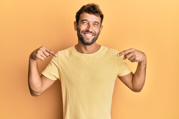 Handsome man with beard wearing casual yellow tshirt over yellow background looking confident with...