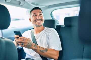 Young hispanic man smiling happy using smartphone sitting on the car.