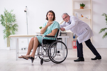 Young male patient in wheel-chair and experienced doctor traumatologist