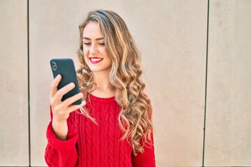 Young blonde girl smiling happy using smartphone standing at the city.