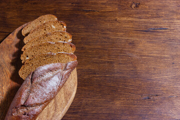 Slices of fresh homemade baguette, bread on a dark wooden board with whole grain, wooden background. Top view with copy space.