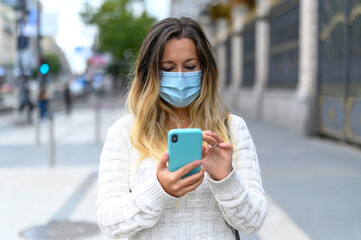 Serious girl with mask checking her phone on street