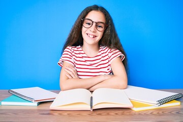 Cute hispanic child girl studying for school exam sitting on the table happy face smiling with crossed arms looking at the camera. positive person.