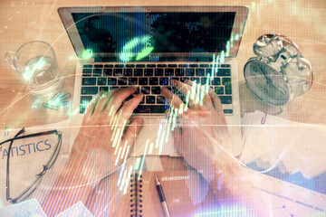 Double exposure of man's hands typing over laptop keyboard and forex chart hologram drawing. Top view. Financial markets concept.