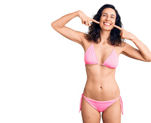 Fototapeta premium Young beautiful hispanic woman wearing bikini smiling cheerful showing and pointing with fingers teeth and mouth. dental health concept.