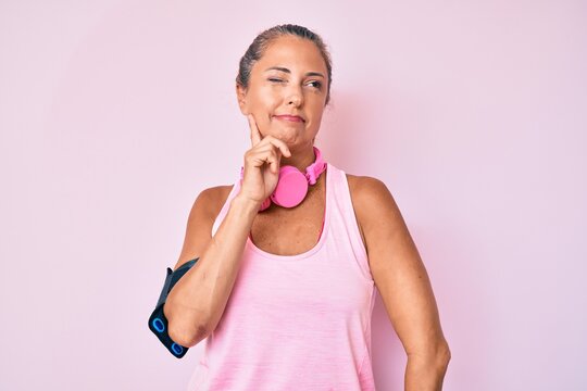 Middle age hispanic woman wearing gym clothes and using headphones serious face thinking about question with hand on chin, thoughtful about confusing idea